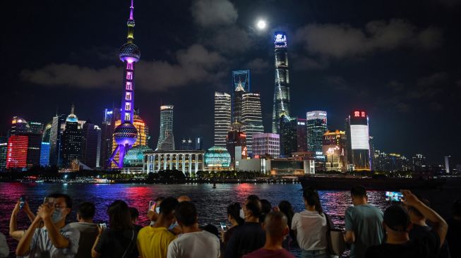 Orang-orang melihat bulan purnama di kawasan sepanjang Sungai Huangpu saat Festival Pertengahan Musim Gugur di Shanghai, China, Sabtu (10/9/2022). [Hector RETAMAL / AFP]