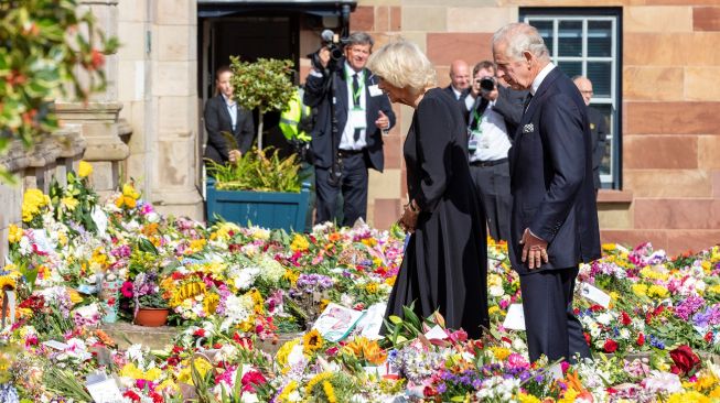 Raja Inggris Charles III dan Permaisuri Camilla melihat karangan bunga yang diberikan masyarakat di luar Kastil Hillsborough, Belfast, Irlandia Utara, Selasa (13/9/2022). [Niall Carson / POOL / AFP]