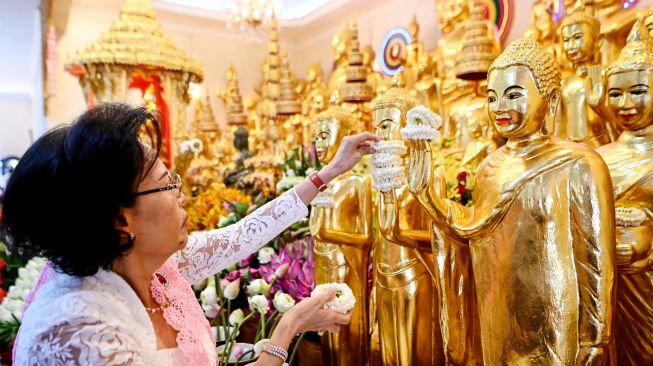 Seorang wanita meletakkan bunga di tangan patung Buddha selama festival Pchum Ben (Festival Kematian) di sebuah pagoda di Phnom Penh, Kamboja, Selasa (13/9/2022). [TANG CHHIN Sothy / AFP]
