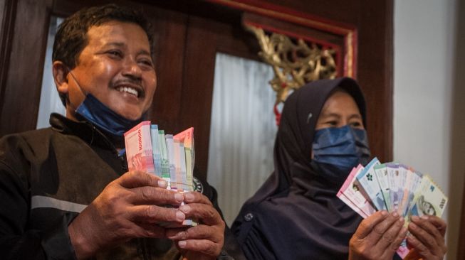 Samin (kiri) beserta istri Sri Kadarwati (kanan) menunjukkan uang baru tahun emisi 2022 usai menukarkan uang rusak miliknya yang dimakan rayap di kantor Perwakilan Bank Indonesia, Solo, Jawa Tengah, Kamis (15/9/2022). [ANTARA FOTO/Mohammad Ayudha/rwa].