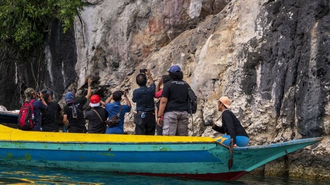 Sejumlah pengunjung memotret cap tangan yang melekat di bebatuan di kawasan Batu Putih, Teluk Tomori, Morowali Utara, Sulawesi Tengah, Kamis (15/9/2022). [Antara Foto]
