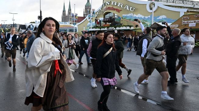 Para pegunjung berlarian menuju tenda bir saat acara festival bir Oktoberfest di lapangan pameran Theresienwiese di Munich, Jerman, Sabtu (17/9/2022). [Christof STACHE / AFP]
