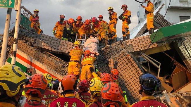 Petugas pemadam kebakaran mengevakuasi seseorang warga dari bangunan runtuh saat operasi penyelamatan akibat gempa bumi di Hualien, Taiwan, Minggu (18/9/2022). [Handout / National Fire Agency / AFP]
