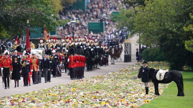 Warga Inggris menyaksikan iring-iringan yang membawa peti mati Ratu elizabeth II saat tiba di Kastil Windsor, Inggris, Senin (19/9/2022). [Andrew Matthews / POOL / AFP]