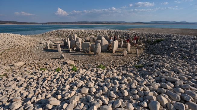 Turis mengunjungi situs megalitik Dolmen of Guadalperal yang muncul kembali setelah air Waduk Valdecanas surut akibat kekeringan yang melanda di Peraleda de la Mata, Spanyol, Kamis (28/8/2022). [PIERRE-PHILIPPE MARCOU / AFP ]
