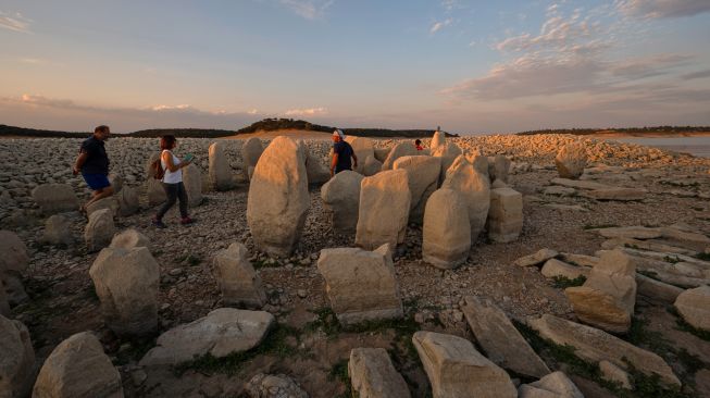 Turis mengunjungi situs megalitik Dolmen of Guadalperal yang muncul kembali setelah air Waduk Valdecanas surut akibat kekeringan yang melanda di Peraleda de la Mata, Spanyol, Kamis (28/8/2022). [PIERRE-PHILIPPE MARCOU / AFP ]
