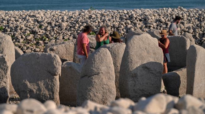 Turis mengunjungi situs megalitik Dolmen of Guadalperal yang muncul kembali setelah air Waduk Valdecanas surut akibat kekeringan yang melanda di Peraleda de la Mata, Spanyol, Kamis (28/8/2022). [PIERRE-PHILIPPE MARCOU / AFP ]
