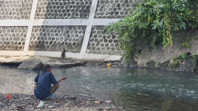 Seorang warga memancing di bantaran Sungai Code yang berada tepatnya bawah Jembatan Gondolayu, Kota Yogyakarta. [Hiskia Andika Weadcaksana / SuaraJogja.id]