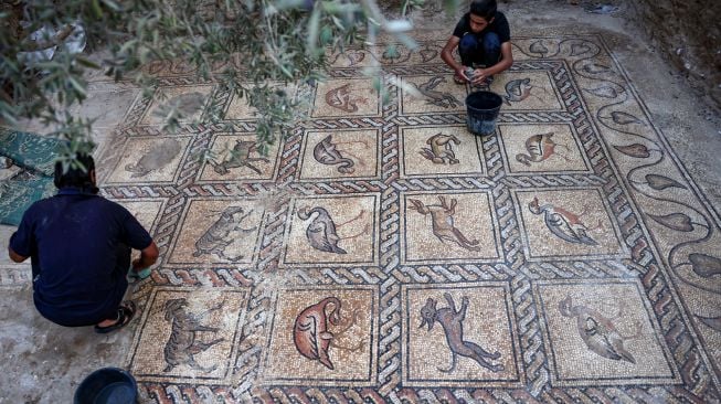 Petani Palestina Salman al-Nabahin dan Putranya saat membersihkan mozaik Bizantium yang ditemukan di tanahnya di Bureij, Gaza, Palestina, Minggu (18/9/2022). [AFP PHOTO/MOHAMMED ABED]