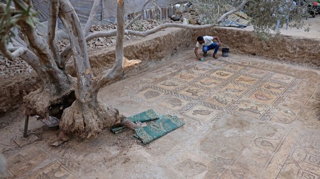 Putra petani Palestina Salman al-Nabahin saat membersihkan mozaik Bizantium yang ditemukan oleh ayahnya ketika menggali tanah di Bureij, Gaza, Palestina, Minggu (18/9/2022). [AFP PHOTO/MOHAMMED ABED]