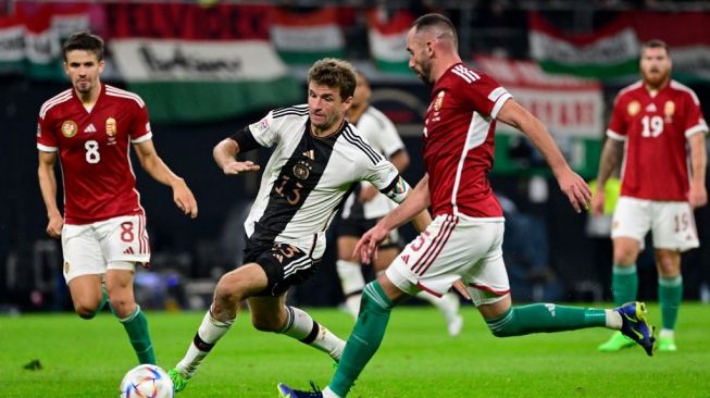 Penyerang Timnas Jerman, Thomas Mueller (tengah) mencoba melepaskan tembakan melewati bek Hungaria Attila Fiola (kanan) selama matchday kelima Grup A3 UEFA Nations League antara Jerman vs Hungaria di Leipzig, Jerman timur pada 23 September 2022.John MACDOUGALL / AFP.