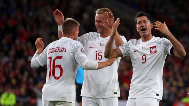 Striker Timnas Polandia Karol Swiderski (kiri) melakukan selebrasi dengan Kamil Glik (tengah) dan striker Robert Lewandowski (kanan) setelah mencetak gol selama matchday keenam atau terakhir Grup A4 UEFA Nations League 2022-2023 antara Wales vs Polandia di stadion Cardiff City di Cardiff, Wales selatan pada 25 September 2022.Geoff Caddick / AFP.