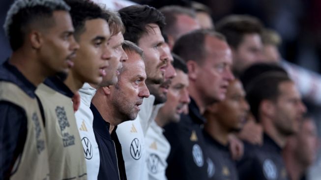O técnico da Alemanha, Hansi Flick (centro), canta o hino nacional antes da partida. [Ronny Hartmann / AFP]