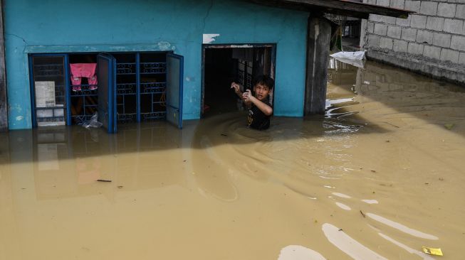 Seorang warga memasuki rumahnya yang terendam banjir setelah terjangan Topan Noru di San Ildefonso, Provinsi Bulacan, Filipina, Senin (26/9/2022). [Ted ALJIBE / AFP]