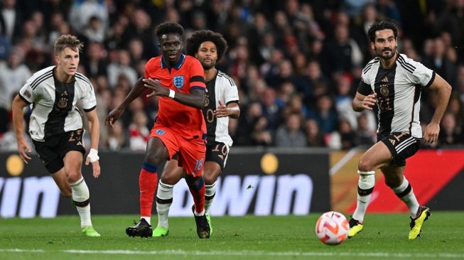 Gelandang Timnas Inggris Bukayo Saka (tengah) bersaing dengan gelandang Jerman Ilkay Gundogan (kanan) selama matchday keenam Grup A3 UEFA Nations League 2022-2023 antara Inggris vs Jerman di stadion Wembley di London utara pada 26 September 2022. Glyn KIRK / AFP.