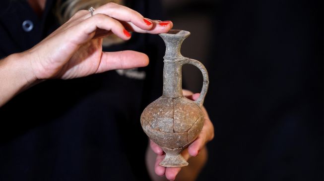 Petugas dari Israel Antiquities Authority (IAA) memegang salah satu bejana yang diyakini berisi opium dari abad ke-14 SM yang ditemukan di situs pemakaman Tel Yehud dan sekarang dipajang di kantor IAA di Yerusalem, Israel, Selasa (20/9/2022). [AHMAD GHARABLI/AFP]