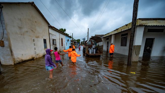 Orang-orang berjalan melewati banjir di jalan yang banjir akibat Badai Ian di Batabano, Kuba, Selasa (27/9/2022). [YAMIL LAGE/AFP]
