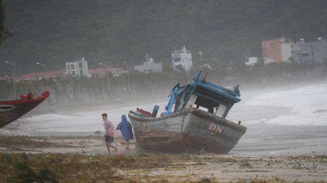 Anak-anak bermain di samping perahu yang terdampar gegera topan Noru di kota Hoi An, provinsi Quang Nam pada Rabu (28/9/2022). [Foto: Nhac NGUYEN / AFP]