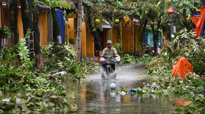 Seorang pria mengendarai sepeda motor di jalan yang tergenang banjir gegera topan Noru di kota Hoi An, provinsi Quang Nam pada Rabu (28/9/2022). [Foto: Nhac NGUYEN / AFP]