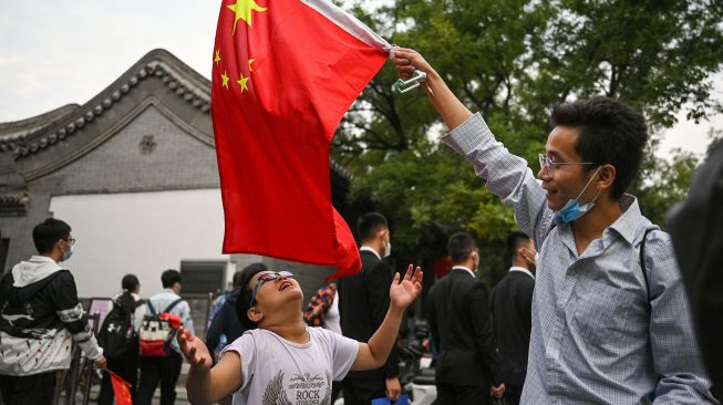 Seorang pria mengibarkan bendera nasional China di Lapangan Tiananmen setelah upacara pengibaran bendera pada Hari Nasional China di Beijing, Sabtu (1/20/2022). [Noel SELIS / AFP]