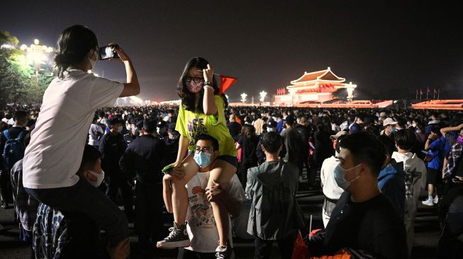 Orang-orang berpose untuk foto di Lapangan Tiananmen saat mereka berkumpul untuk upacara pengibaran bendera pada Hari Nasional China di Beijing, Sabtu (1/20/2022). [Noel SELIS / AFP]