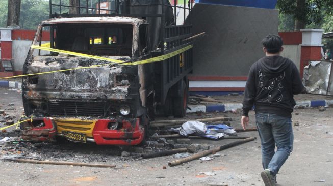 Seorang warga melintas di samping mobil yang terbakar pasca kerusuhan di Stadion Kanjuruhan, Malang, Jawa Timur, Minggu (2/10/2022). [ANTARA FOTO/Ari Bowo Sucipto/foc]