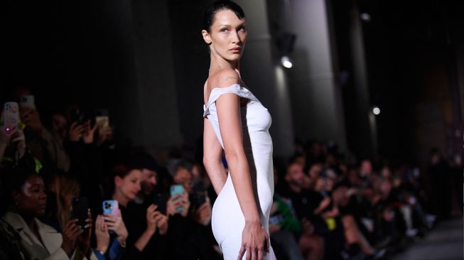 Model Bella Hadid tampil di catwalk dengan slip dress yang disemprot dengan kain Fabrican Spray-on selama peragaan busana Coperni Spring-Summer 2023 yang merupakan bagian dari Paris Fashion Week di Paris, Prancis, Jumat (30/9/2022). [JULIEN DE ROSA / AFP]