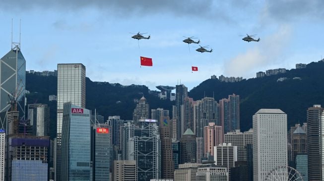 Helikopter terbang dengan bendera Hong Kong dan China untuk memperingati Hari Nasional China di Hongkong, Sabtu (1/10/2022). [Peter PARKS/AFP]
