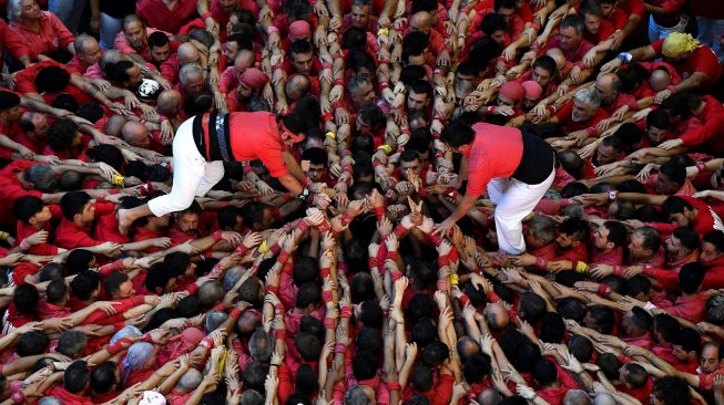 Anggota tim menara manusia "Jove de Valls" berusaha membentuk "castell" (menara manusia) selama kompetisi 'castells' edisi ke-28 di arena Tarraco di Tarragona, Catalunya, Spanyol, Minggu (2/10/2022). [Josep LAGO / AFP]
