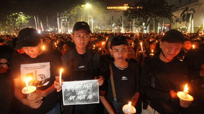 Suporter Persebaya memegang lilin saat mengikuti doa bersama di Tugu Pahlawan, Surabaya, Jawa Timur, Senin (3/10/2022).  ANTARA FOTO/Didik Suhartono