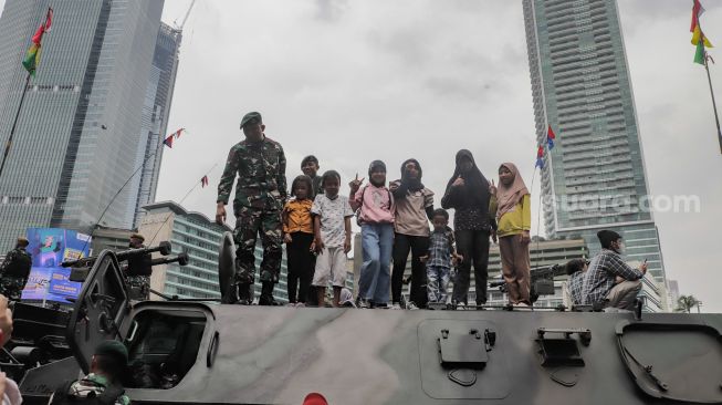 Warga berswafoto dengan kendaraan alutsista milik TNI yang dipamerkan di Bundaran HI, Jakarta Selatan, Rabu (5/10/2022). [Suara.com/Alfian Winanto]