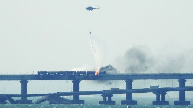 Sebuah helikopter berusaha memadamkan api kebakaran akibat sebuah truk yang meledak di jembatan Kerch yang menghubungkan Krimea dan Rusia di semenanjung Kerch, Sabtu (8/10/2022). [Foto oleh AFP]