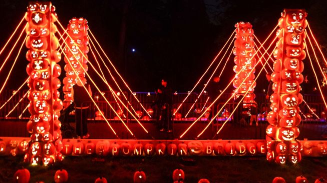 Pengunjung melintasi Jembatan labu di pameran Great Jack O'Lantern Blaze di Van Cortlandt Manor, Croton-on-Hudson, New York, Amerika Serikat, Sabtu (8/10/2022). [Bryan R. Smith / AFP]