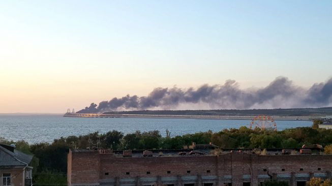 Asap hitam mengepul dari kebakaran akibat sebuah truk yang meledak di jembatan Kerch yang menghubungkan Krimea dan Rusia di semenanjung Kerch, Sabtu (8/10/2022). [Anna Karpenko / AFP]
