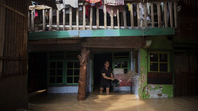 Warga membersihkan tembok rumahnya saat banjir di Taman Harapan, Cawang, Kramat Jati, Jakarta Timur, Rabu (12/10/2022). [ANTARA FOTO/Sigid Kurniawan/foc].