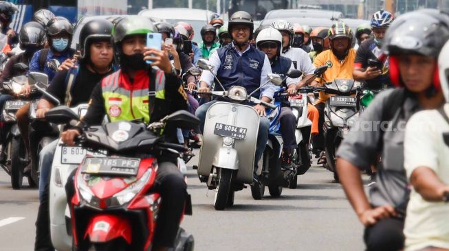 Gubernur DKI Jakarta Anies Baswedan (tengah) menaiki sepeda motor vespa saat melintas di Jalan Jenderal Sudirman, Jakarta Pusat, Minggu (16/10/2022). [Suara.com/Alfian Winanto]