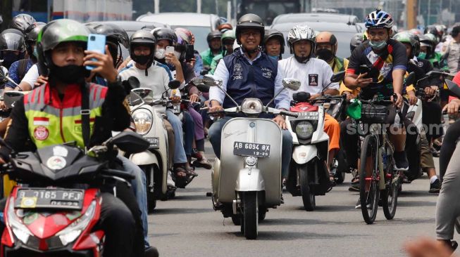 Gubernur DKI Jakarta Anies Baswedan (tengah) menaiki sepeda motor vespa saat melintas di Jalan Jenderal Sudirman, Jakarta Pusat, Minggu (16/10/2022). [Suara.com/Alfian Winanto]