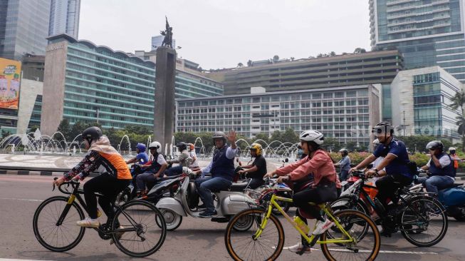 Gubernur DKI Jakarta Anies Baswedan (tengah) menaiki sepeda motor vespa saat melintas di Jalan Jenderal Sudirman, Jakarta Pusat, Minggu (16/10/2022). [Suara.com/Alfian Winanto]