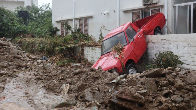 Sebuah truk pick-up tersangku di dinding akibat banjir bandang yang melanda di Agia Pelagia, Pulau Kreta, Yunani, Sabtu (15/10/2022). [Costas METAXAKIS / AFP]