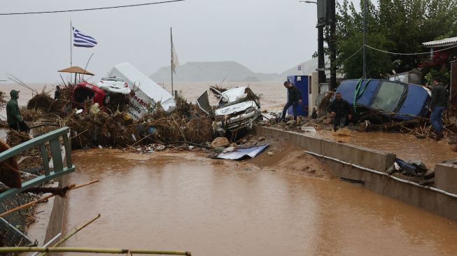 Petugas pemadam kebakaran dan warga melihat kerusakan akibat banjir bandang yang melanda di desa Agia Pelagia,  Pulau Kreta, Yunani, Sabtu (15/10/2022). [Costas METAXAKIS / AFP]