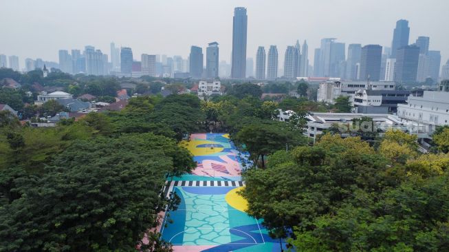 Anak-anak bermain basket di atas mural karya seniman grafiti Stereoflow alias Adi Dharma di Lapangan Taman Menteng, Jakarta Pusat, Rabu (18/10/2022). [Suara.com/Alfian Winanto]