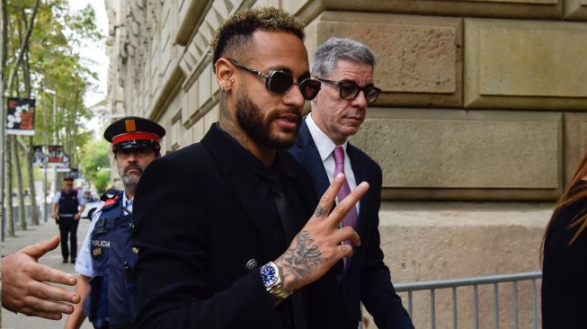 Pesepak bola Paris Saint-Germain Neymar menyapa awak media usai menghadiri sidang di gedung pengadilan di Barcelona, Spanyol, Senin (17/10/2022). [Pau BARRENA / AFP]