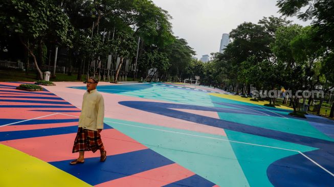 Warga berjalan di atas mural karya seniman grafiti Stereoflow alias Adi Dharma di Lapangan Taman Menteng, Jakarta Pusat, Rabu (18/10/2022). [Suara.com/Alfian Winanto]