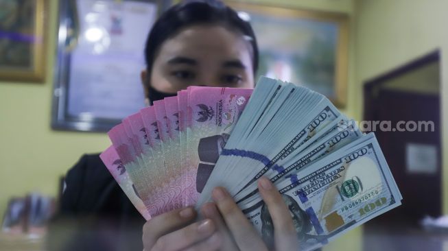 Petugas menunjukkan mata uang Rupiah dan Dolar AS di tempat penukaran uang Dolar Indo, Jakarta, Kamis (20/10/2022). [Suara.com/Alfian Winanto]