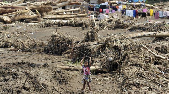 Seorang anak bermain di area rumahnya yang dipenuhi material kayu dan lumpur pascabanjir bandang di lingkungan Bilukpoh, Kelurahan Tegal Cangkring, Jembrana, Bali, Jumat (21/10/2022). [ANTARA FOTO/Nyoman Hendra Wibowo/nz]