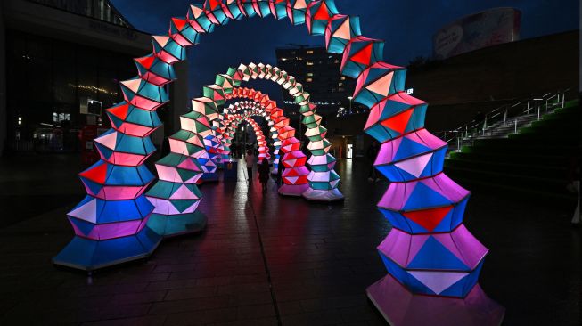 Warga berjalan melintasi karya seni berjudul "Rainbow Accordion" oleh studio desain Amigo & Amigo yang dipamerkan saat festival River of light di Liverpool, Inggris, Kamis (20/10/2022). [Paul ELLIS / AFP]