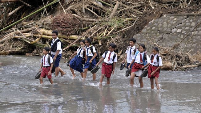 Sejumlah siswa menyeberangi sungai saat berangkat ke sekolah pascabanjir bandang di Dusun Sekar Kejula Kelod, Desa Yehembang Kauh, Jembrana, Bali, Selasa (25/10/2022). [ANTARA FOTO/Nyoman Hendra Wibowo/hp].