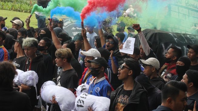 Sejumlah warga dan suporter Arema FC (Aremania) menyalakan api suar atau flare saat berunjuk rasa di depan Balai Kota Malang, Jawa Timur, Kamis (27/10/2022). Selain menuntut penuntasan kasus tragedi Kanjuruhan yang transparan dan adil, mereka juga meminta pihak terkait pelaksana liga yakni PSSI dan pemegang hak siar pertandingan Arema FC lawan Persebaya turut bertanggung jawab dalam tragedi yang menewaskan 135 orang tersebut. [ANTARA FOTO/Ari Bowo Sucipto/nym].