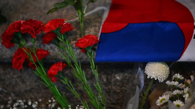 Bunga dan bendera Korea Selatan untuk penghormatan kepada para korban dalam tragedi Itaewon di luar stasiun kereta bawah tanah Itaewon, Seoul, Korea Selatan, Minggu (30/10/2022). [Anthony WALLACE / AFP]