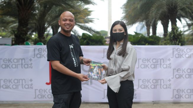 Wakil Mentri Pariwisata dan Ekonomi Kreatif Angela Tanoesoedibjo menerima buku foto Rekam Jakarta 24+ yang diberikan Ketua PFI Jakarta Herman Zakharia saat mengunjungi pameran foto jurnalistik Rekam Jakarta 24+ di Taman Lapangan Banteng, Jakarta, Selasa (1/11/2022). [Dok. PFI Jakarta]